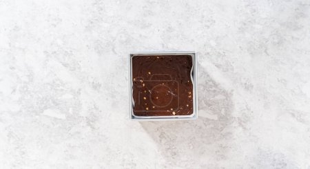 Téléchargez les photos : Pose plate. Poêle à gâteau au fromage carrée garnie de papier sulfurisé avec mélange de caramel pour préparer le caramel aux noisettes au chocolat. - en image libre de droit