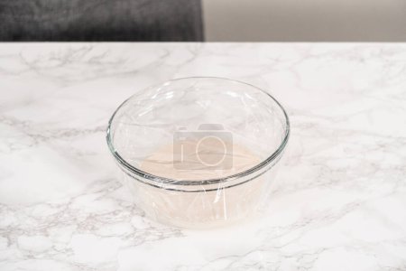Foto de Mezclar los ingredientes en un tazón de vidrio para hornear bollos de brioche caseros. - Imagen libre de derechos