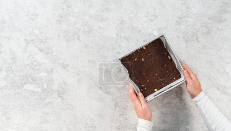 Téléchargez les photos : Pose plate. Fudge macadamia au chocolat fraîchement confectionné dans un moule carré tapissé de papier parchemin. - en image libre de droit