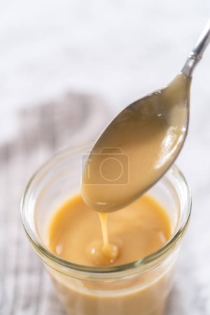 Téléchargez les photos : Glaçage au caramel fait maison dans un bocal en verre sur le comptoir de la cuisine. - en image libre de droit