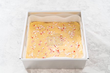 Filling square cheesecake pan lined with parchment paper with fudge mixture to prepare candy cane fudge.