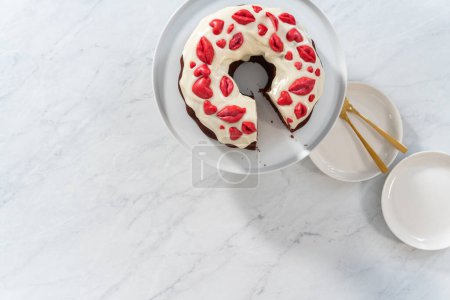 Foto de Flat lay. Slicing freshly baked red velvet bundt cake with chocolate lips and hearts over cream cheese glaze for Valentines Day. - Imagen libre de derechos