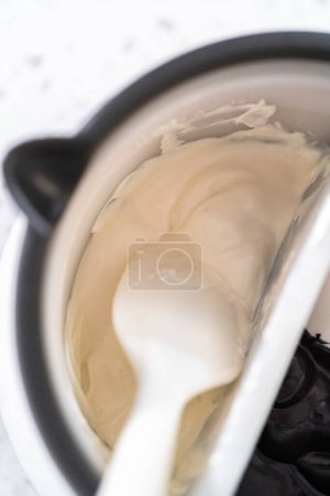 Téléchargez les photos : Fondre des pépites de chocolat dans un melting pot de bonbons pour faire Halloween tiges de bretzel recouvert de chocolat. - en image libre de droit