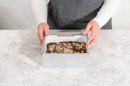 Foto de Filling square cheesecake pan lined with parchment paper with fudge mixture to prepare chocolate hazelnut fudge. - Imagen libre de derechos
