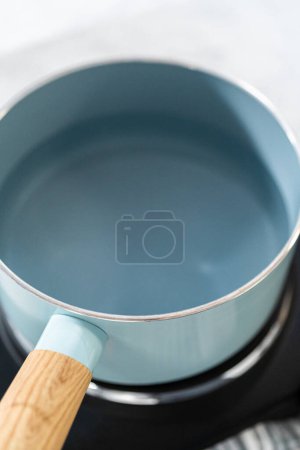 Photo for Melting chocolate chips and other ingredients in a glass mixing bowl over boiling water to prepare chocolate hazelnut fudge. - Royalty Free Image