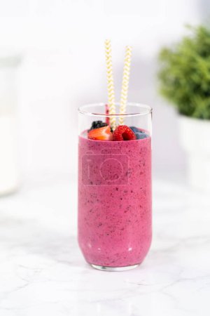 Photo for Freshly made mixed berry smoothie garnished with fresh berries and paper straws. - Royalty Free Image