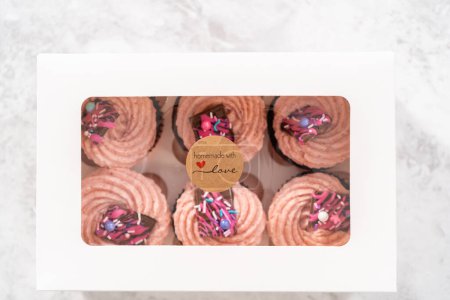 Foto de Embalaje recién horneado cupcakes de chocolate fresa adornado con mini chocolates gourmet rosa en una caja de cupcakes de papel blanco. - Imagen libre de derechos