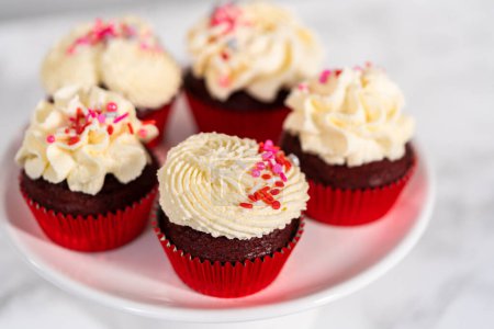 Téléchargez les photos : Cupcakes de velours fraîchement cuits au four avec glaçage ganache au chocolat blanc décoré de saupoudres. - en image libre de droit