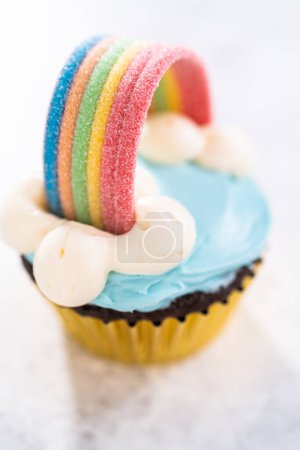 Foto de Pastelitos de chocolate decorados con glaseado de crema de mantequilla azul y arco iris para la fiesta de cumpleaños temática de unicornio. - Imagen libre de derechos