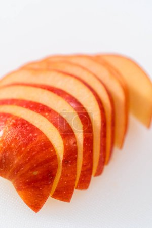 Foto de Cortar manzanas rojas en rodajas finas en una tabla de cortar blanca. - Imagen libre de derechos