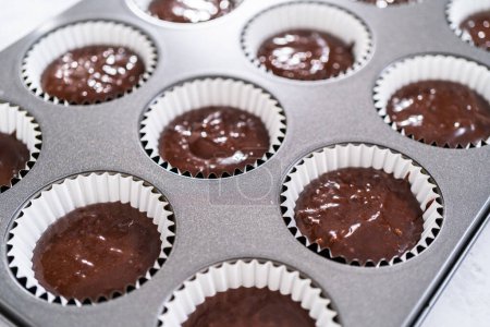 Téléchargez les photos : Ramasser la pâte de cupcake au chocolat dans les doublures de cupcake. - en image libre de droit