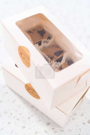 Téléchargez les photos : Emballage de caramel au chocolat fait maison avec du beurre d'arachide tourbillonner dans une boîte cadeau blanche. - en image libre de droit