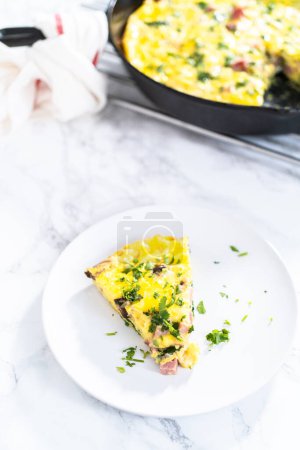 Photo for Slice of spinach and ham frittata on a white dinner plate. - Royalty Free Image