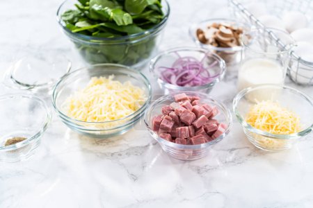 Foto de Ingredientes en cuencos de vidrio para preparar espinacas y jamón frittata. - Imagen libre de derechos