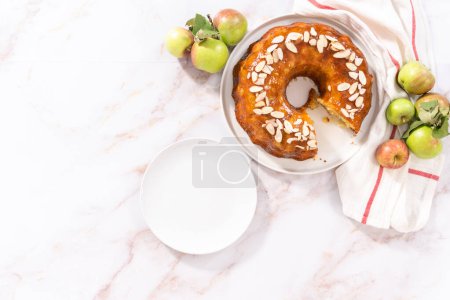 Photo for Flat lay. Slicing homemade apple bundt cake and garnishing with sliced almonds. - Royalty Free Image