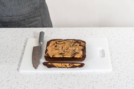 Téléchargez les photos : Couper le caramel au chocolat avec du beurre d'arachide en petits morceaux sur une planche à découper blanche. - en image libre de droit