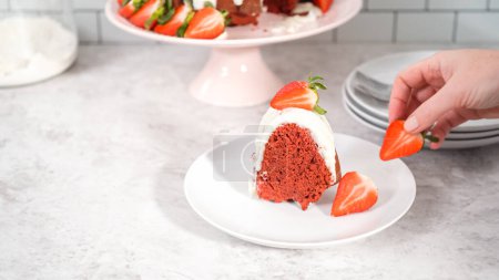 Téléchargez les photos : Pas à pas. Tranche de gâteau bundt en velours rouge avec glaçage au fromage à la crème garnie de fraises fraîches sur une assiette blanche. - en image libre de droit