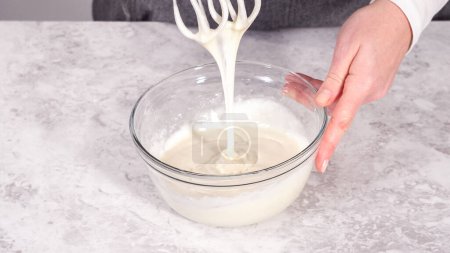 Foto de Paso a paso. Mezclar los ingredientes en un tazón de vidrio para preparar glaseado de queso crema. - Imagen libre de derechos