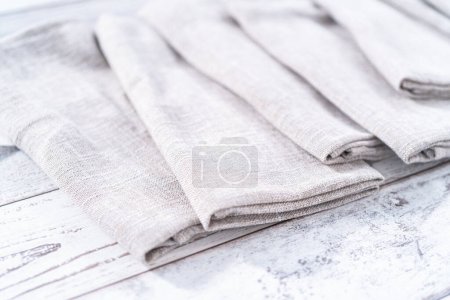 Photo for Closeup view of a natural color linen dinner napkin on a wooden white table. - Royalty Free Image