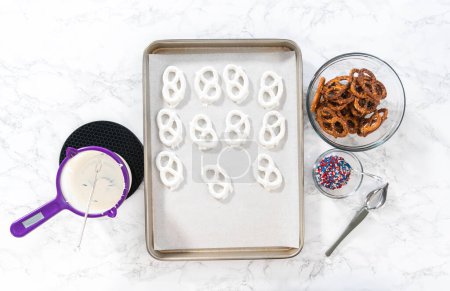 Foto de Flat lay. Dipping pretzels twists into melted chocolate to make red, white, and blue chocolate-covered pretzel twists. - Imagen libre de derechos