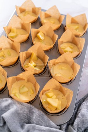 Téléchargez les photos : Ramasser la pâte dans la casserole à cupcake doublée de doublures de muffins en parchemin pour cuire des muffins sharlotka. - en image libre de droit