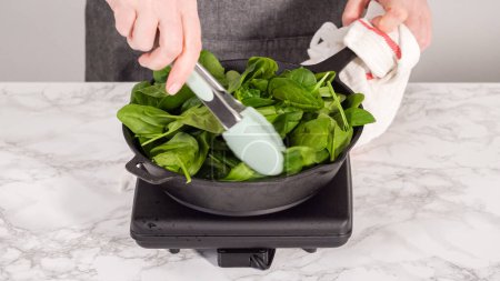 Photo for Step by step. Heating cast iron skillet over the stove to prepare spinach and ham frittata. - Royalty Free Image