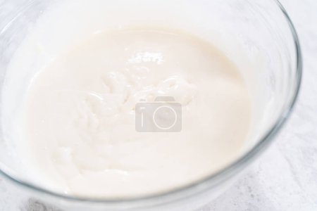 Foto de Mezclar los ingredientes en un tazón de vidrio para preparar glaseado de queso crema. - Imagen libre de derechos