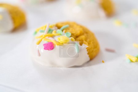 Photo for Lemon Cookies with White Chocolate. Dipping lemon cookies into melted white chocolate and decorating them with Easter sprinkles. - Royalty Free Image