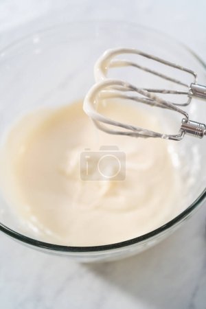 Foto de Mezclar los ingredientes en un tazón de vidrio grande para hacer el glaseado de queso crema. - Imagen libre de derechos