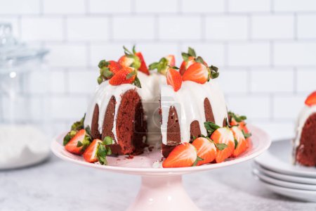 Photo for Slicing red velvet bundt cake with cream cheese frosting garnished with fresh strawberries. - Royalty Free Image