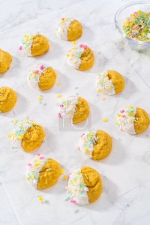 Photo for Lemon Cookies with White Chocolate. Dipping lemon cookies into melted white chocolate and decorating them with Easter sprinkles. - Royalty Free Image