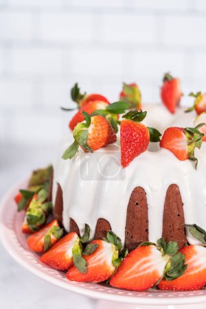 Téléchargez les photos : Fresh strawberries..Red velvet bundt cake with cream cheese frosting garnished with fresh strawberries on a pink cake stand for Valentines Day. - en image libre de droit
