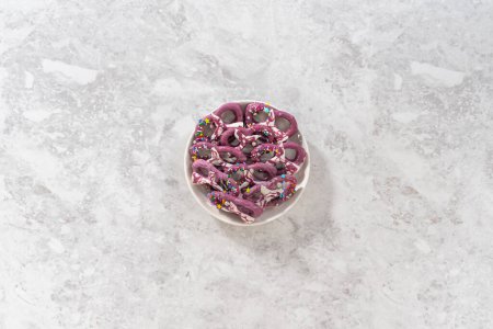 Foto de Flat lay. Homemade chocolate-dipped pretzel twists decorated with colorful sprinkles and chocolate mermaid tails on a white plate. - Imagen libre de derechos