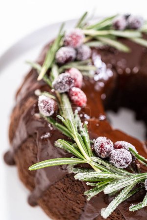 Foto de Tarta de chocolate con glaseado de chocolate decorado con arándanos frescos y romero cubierto con azúcar blanca. - Imagen libre de derechos