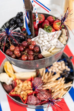 Photo for July 4th charcuterie board on a two-tiered serving metal stand filled with cheese, crackers, salami, and fresh fruits - Royalty Free Image