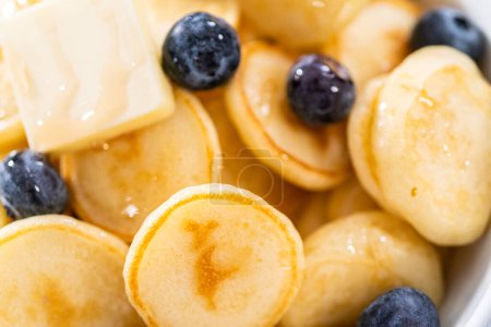 Téléchargez les photos : Mini céréales crêpes fraîchement préparées avec des bleuets frais dans un bol blanc. - en image libre de droit