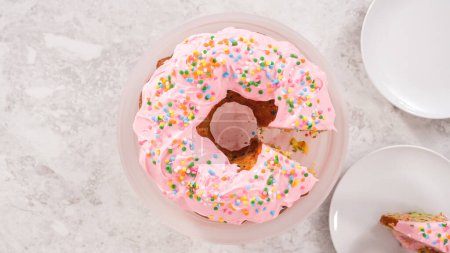 Téléchargez les photos : Pose plate. Pas à pas. Gâteau funfettti Bundt tranchant avec glaçage à la crème au beurre rose sur le dessus et remplissage à la crème au beurre à l'intérieur. - en image libre de droit