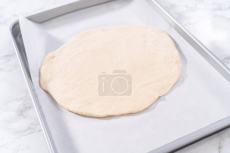 Preparación de pizza de postre de canela en una bandeja para hornear forrada con papel pergamino.