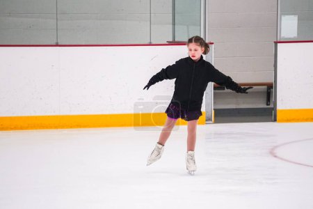 Téléchargez les photos : Petite fille pratiquant avant sa compétition de patinage artistique à la patinoire intérieure. - en image libre de droit