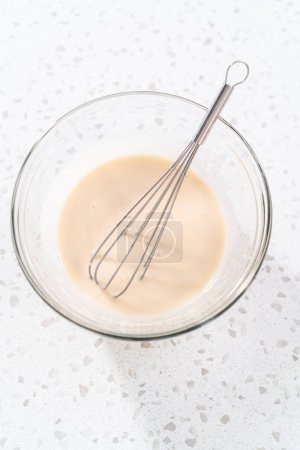Foto de Mezclar los ingredientes con un batidor de mano en un recipiente de vidrio para hacer que el esmalte de vainilla. - Imagen libre de derechos