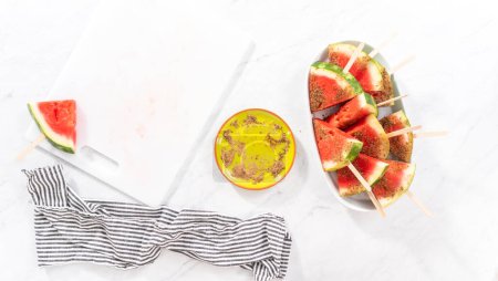 Photo for Flat lay. Dipping watermelon pops into the chili lime salt to prepare Mexican watermelon pops. - Royalty Free Image