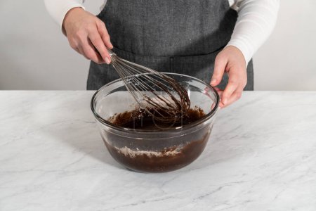 Foto de Mezclar ingredientes húmedos y secos con un batidor de mano en un tazón de vidrio para hornear brownies de menta. - Imagen libre de derechos