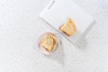 Téléchargez les photos : Pose plate. Sandwichs au jambon, concombre et germe sur la planche à découper blanche. - en image libre de droit
