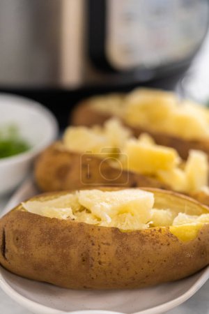Téléchargez les photos : Pommes de terre cuites au four Pressure Cooker. Trancher les pommes de terre entières cuites sur une assiette blanche pour faire des pommes de terre cuites au four. - en image libre de droit