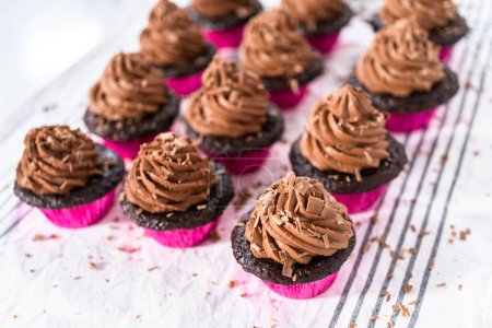 Téléchargez les photos : Piping chocolat ganache glaçage sur le dessus de cupcakes au chocolat. - en image libre de droit