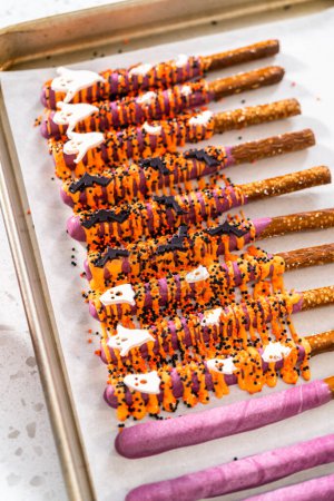 Photo for Dipping pretzel rods into melted chocolate to make Halloween chocolate-covered pretzel rods. - Royalty Free Image