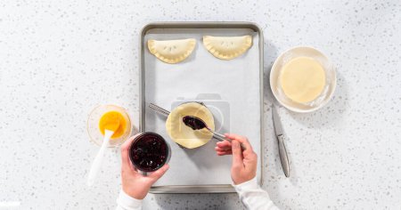 Photo for Flat lay. Filling empanada dough with blueberry pie filling to make sweet empanadas with blueberries. - Royalty Free Image