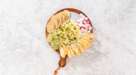 Photo for Flat lay. Assembling butter board with vegetables and bread on a round wood cutting board. - Royalty Free Image