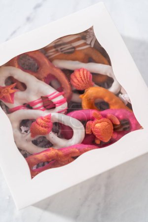 Photo for Packaging gourmet chocolate-covered pretzel twists into a white paper gift box filled with paper shreds. - Royalty Free Image