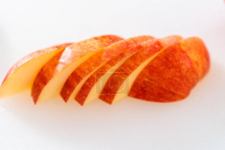 Foto de Cortar manzanas rojas en rodajas finas en una tabla de cortar blanca. - Imagen libre de derechos